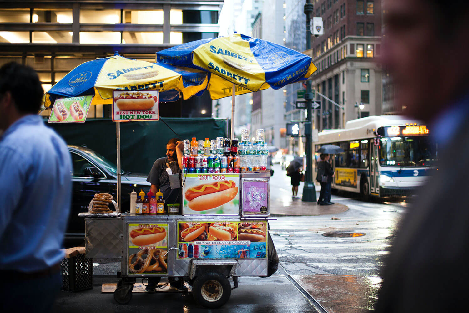 A New York City hotdog street vendor leaning on his hotdog cart on a rainy day