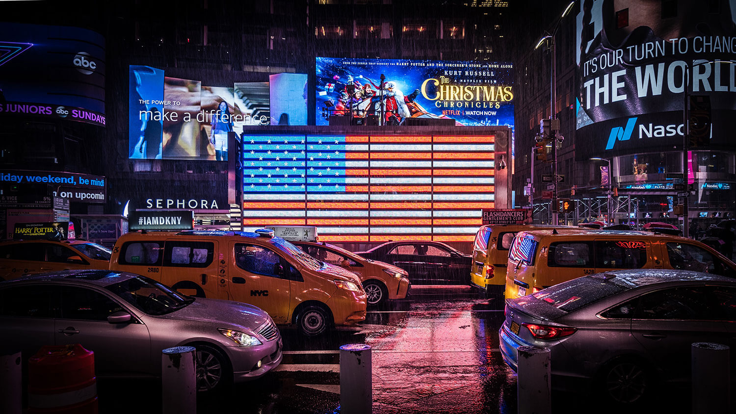 Traffic stopped in the rain in New York in front of a large illuminated American flag