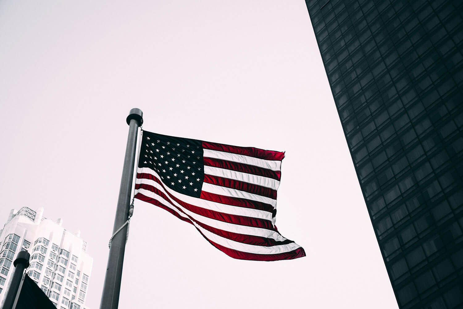 American flag waving in the wind on a flagpole with tall buildings in the background