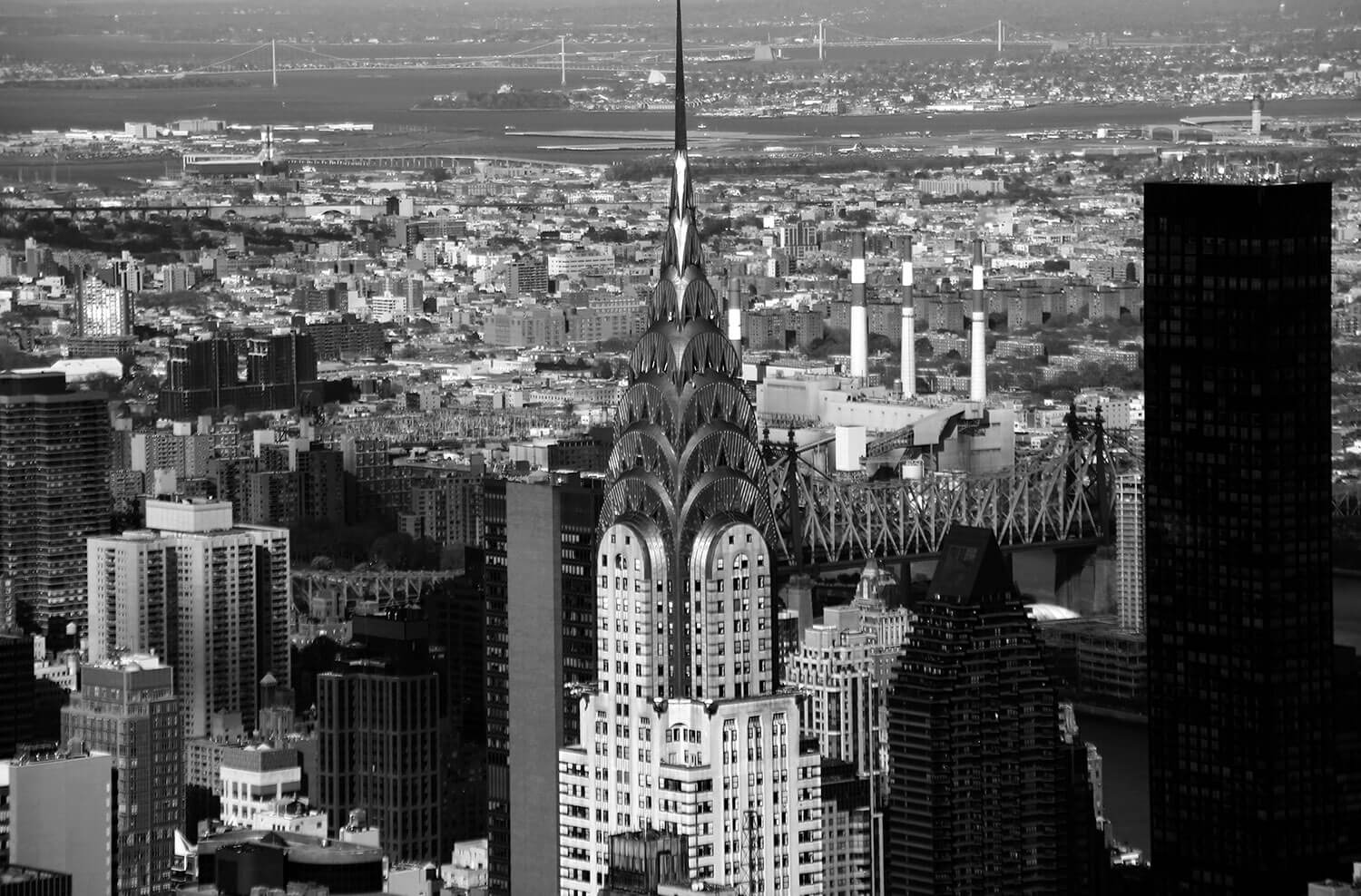 Black and white photo of the top of the Empire State building surrounded by other skyscrapers